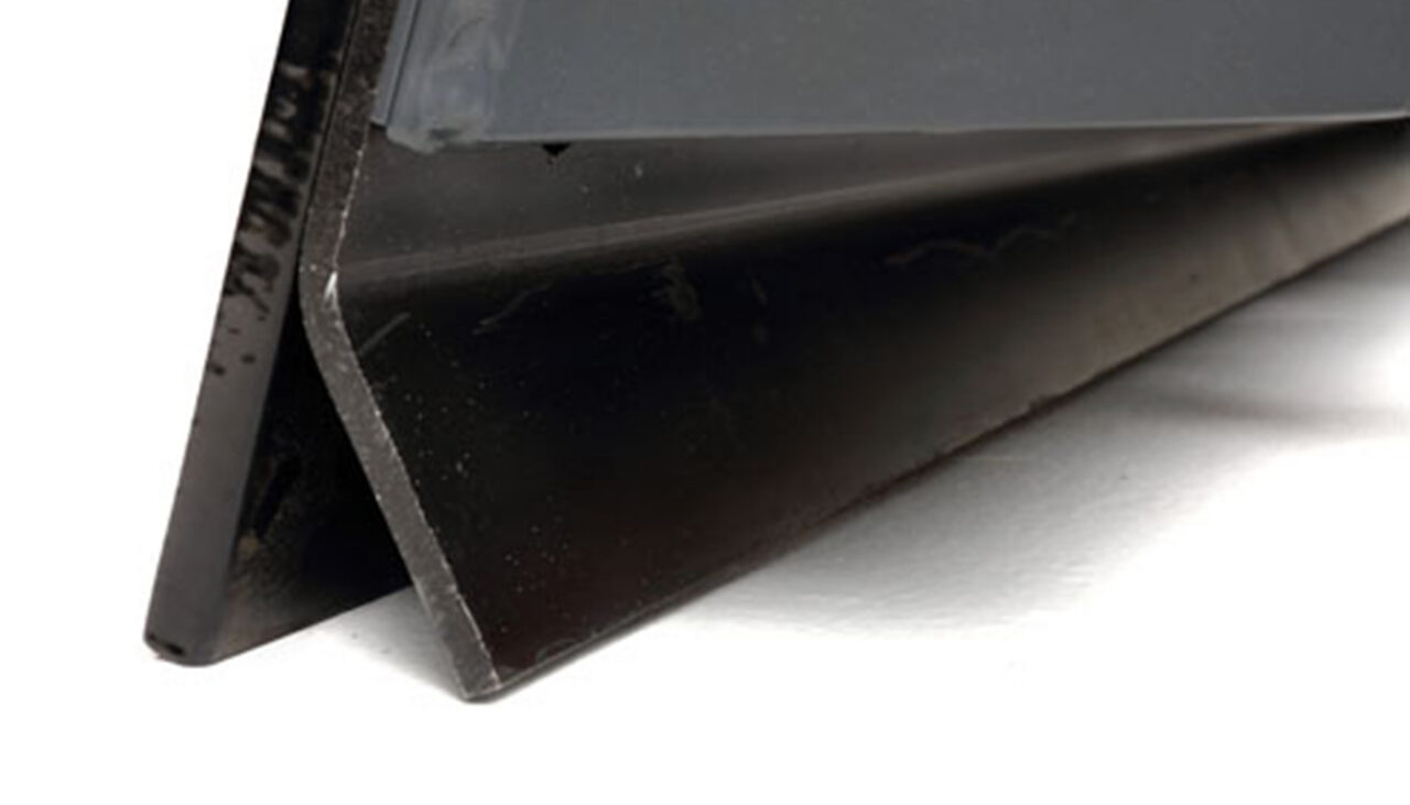 Close-up of a black metal angle iron, positioned on a white surface with one edge facing the camera, showing its L-shaped cross-section.